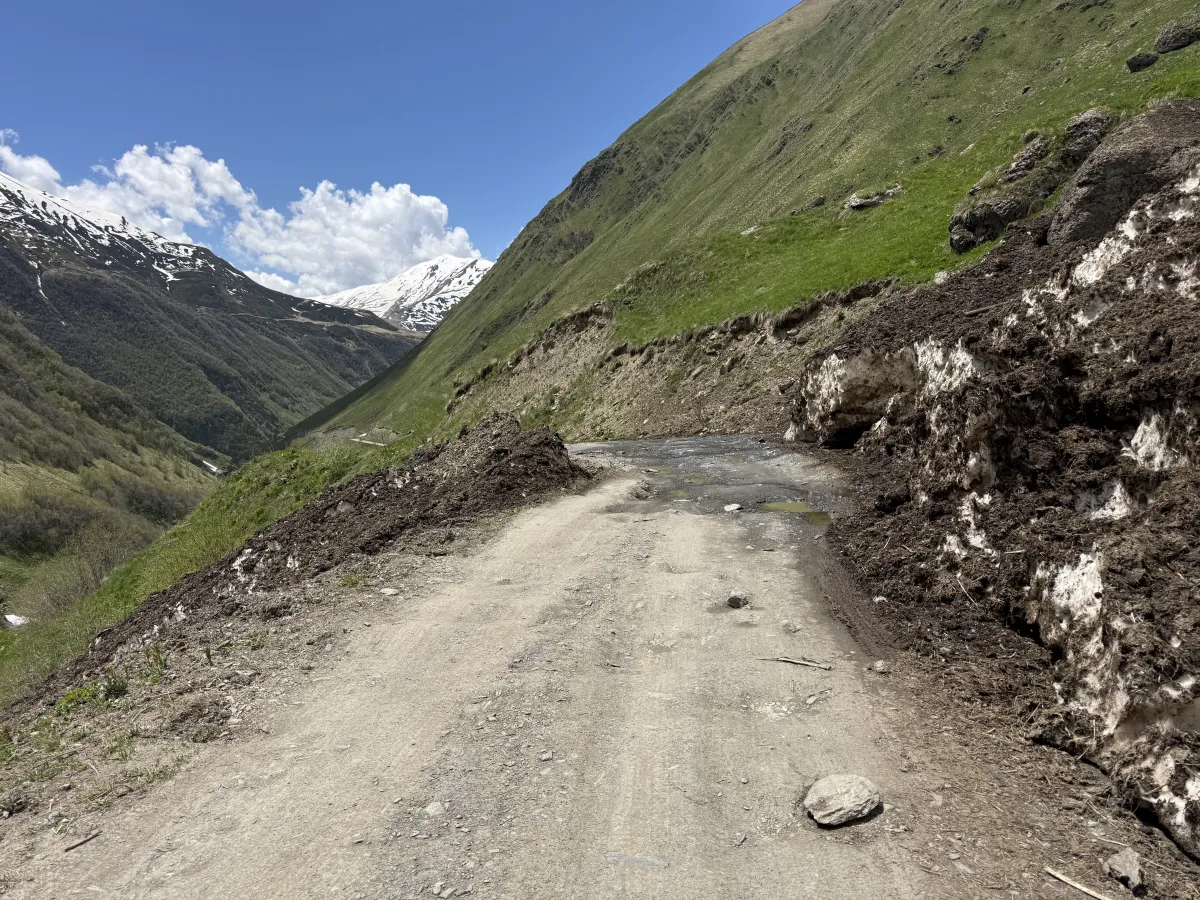 Muddy single-lane stretch of road squeezed between banks of dirty avalanche snow