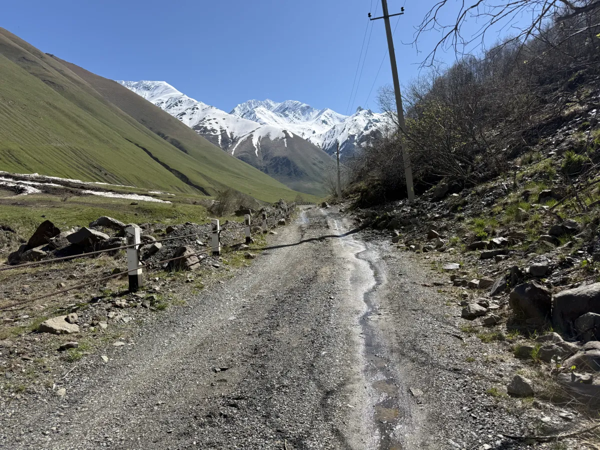 Wet stony road with meltwater running down it just past Juta, snowy peaks behind