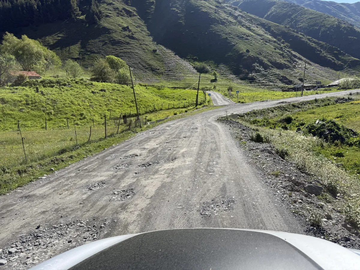 Potholed gravel road descending past farm buildings in the Sno valley