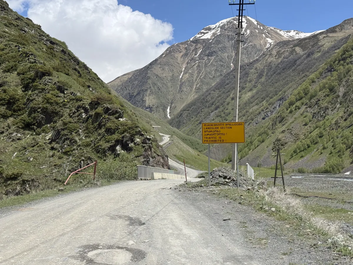 Gravel road crossing a small bridge next to a yellow landslide-section warning sign