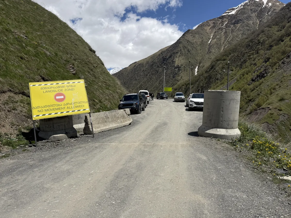 Cars parked by concrete blocks at a wide gravel spot in the mountain valley