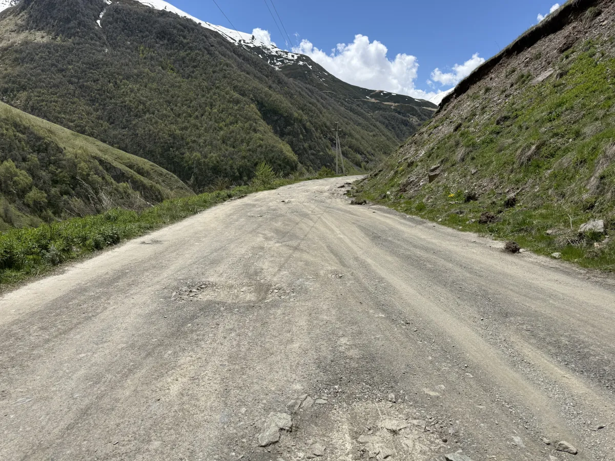Broad rutted gravel road climbing beside a steep earth cut bank