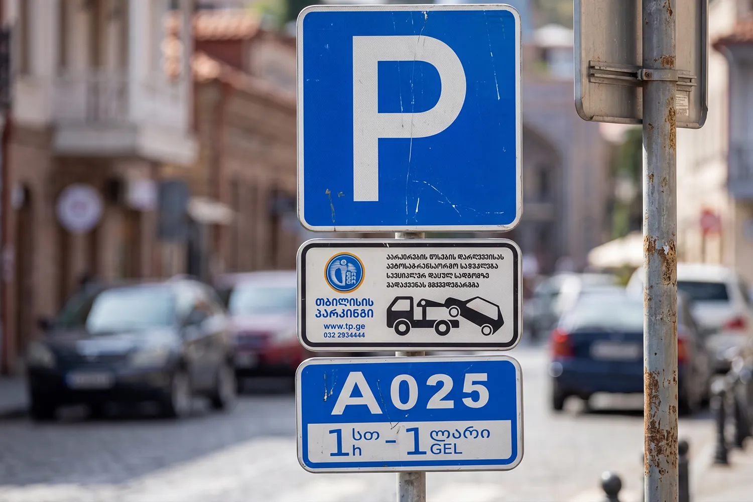 Close-up of a Tbilisi hourly zonal parking sign — a blue P over a white plate marked 'A722' — mounted on a street pole in central Tbilisi.
